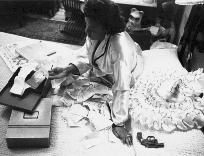 Icon Fannie Mae sits on a bed looking over paperwork